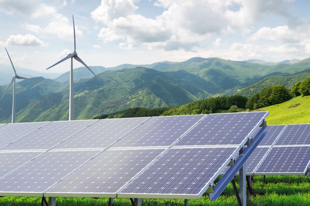 Pannelli fotovoltaici e pale eoliche su sfondo montano