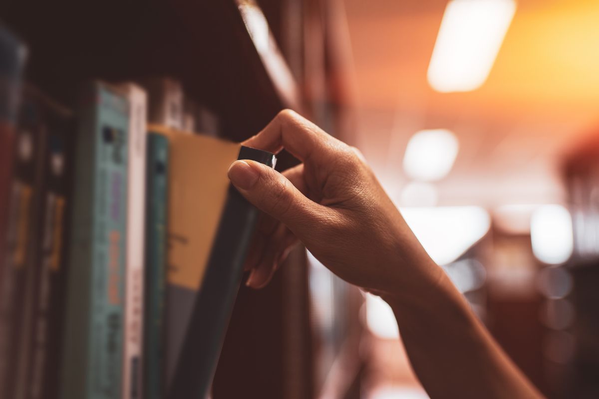 Una donna prende un libro dallo scaffale di una biblioteca