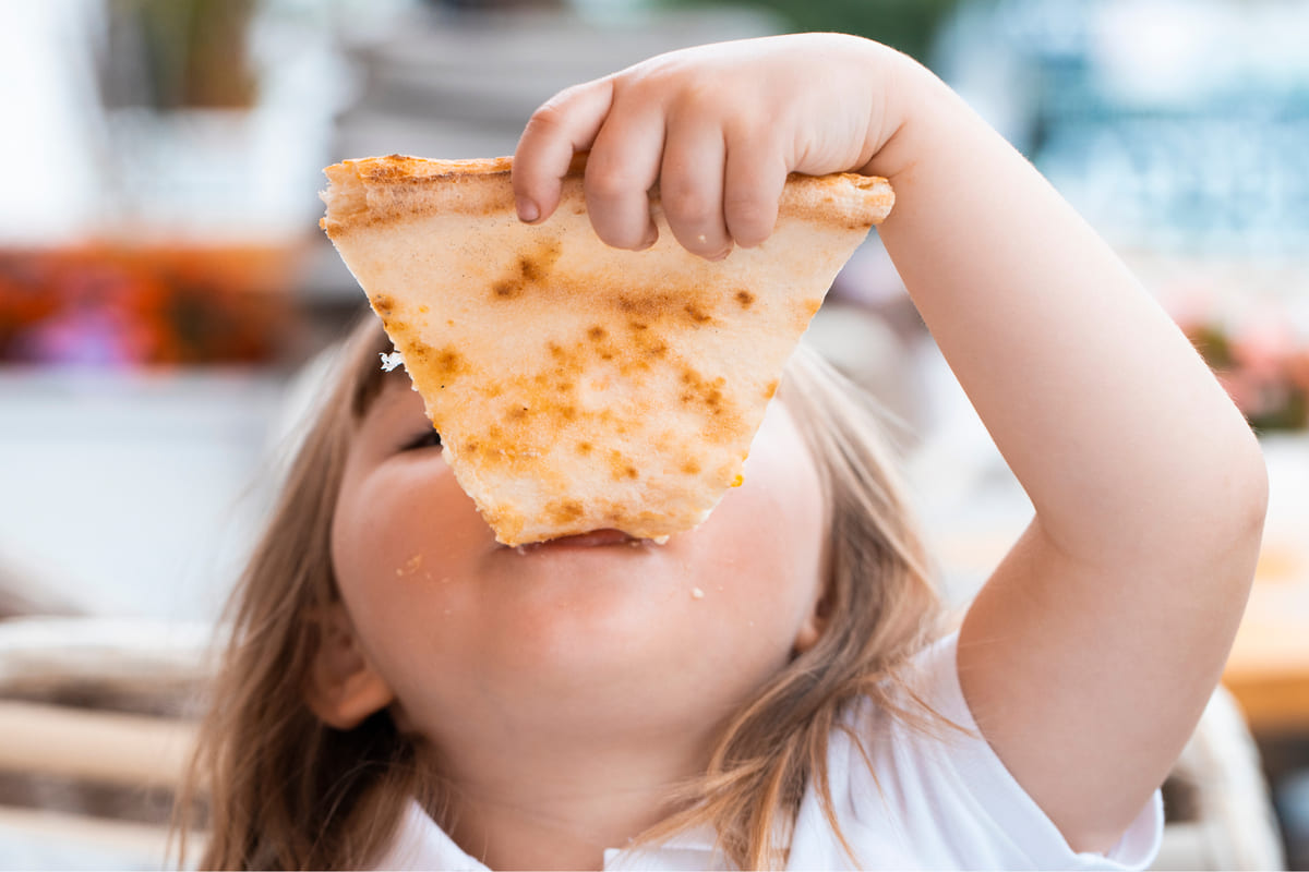 Una bambina mangia una fetta di pizza
