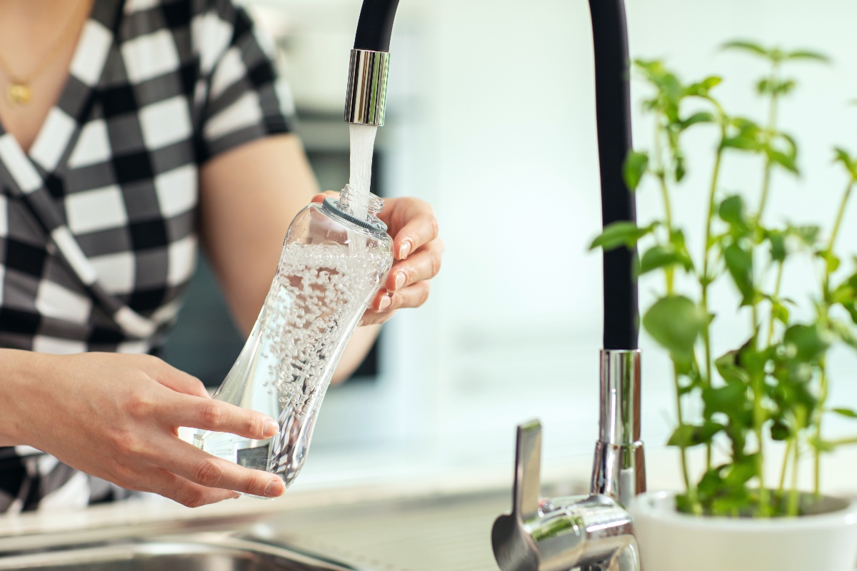 Una donna riempie una bottiglia dall'acqua del rubinetto