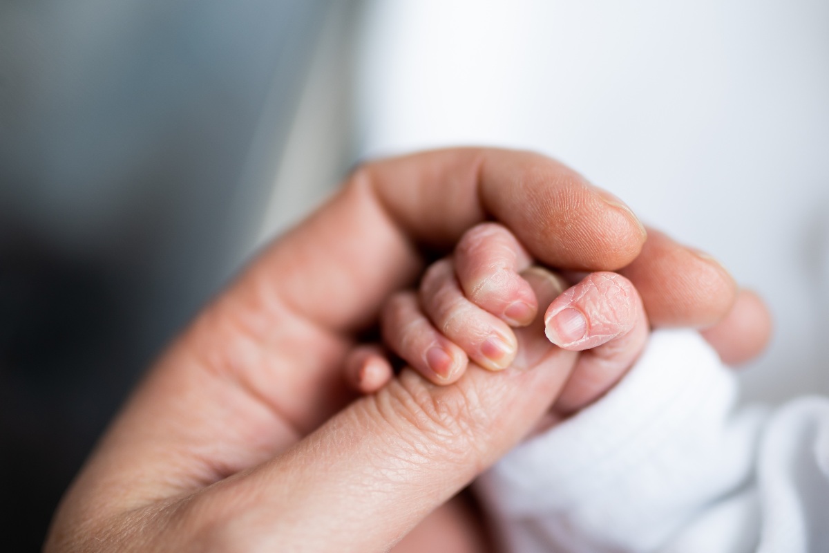 Un neonato stringe la mano di un adulto